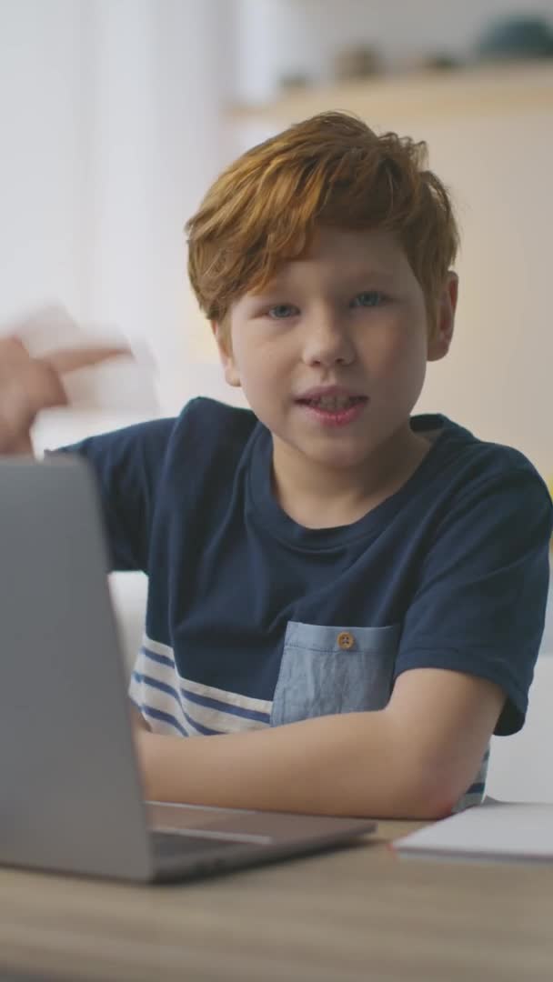 Generation Z. Liten rödhårig pojke hälsning, viftande hand till kamera, sitter med laptop hemma, video för vertikal berättelse — Stockvideo