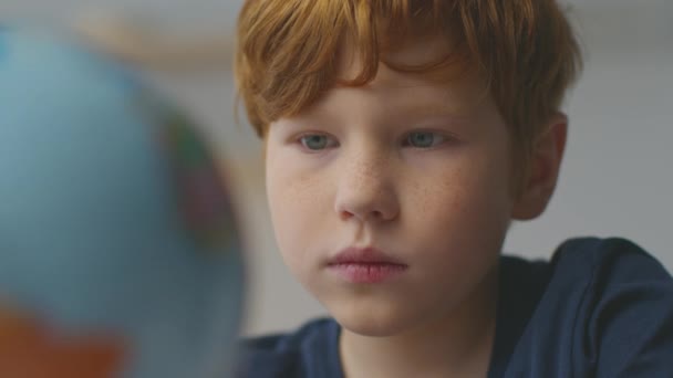 Interesting geography. Close up portrait of cute little redhead boy searching globe at home, looking at world map — Wideo stockowe