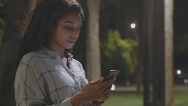 Aplicación de redes sociales de moda. Jóvenes afroamericanos mujer web surf en internet, mensajería en línea en el parque nocturno — Vídeo de stock