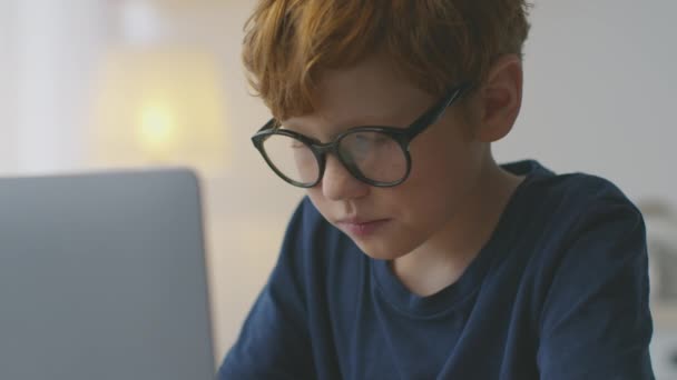 Desenvolvimento e educação de crianças. Pouco concentrado ruiva estudante nerd estudando em casa no laptop, câmera lenta — Vídeo de Stock