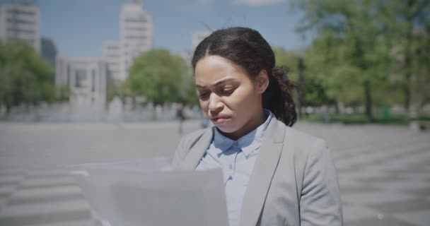 Problemi con il flusso dei documenti. Donna afro-americana disturbata che legge giornali all'aperto, ha trovato errori, inseguimento. — Video Stock