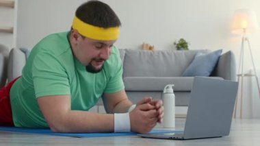 Sportif yaşam tarzının başlangıcı. Kişisel koçla internetten şişman adam antrenmanı yapıyor, laptopunu selamlıyor ve kalas yapıyor.