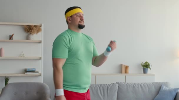 Sports activity. Chubby man in bright sport clothes exercising with small dumbbells at home, free space, slow motion — Stock video