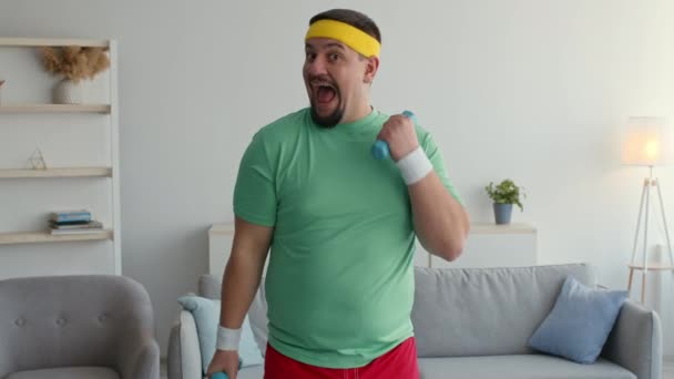 Expressive funny overweight man in bright sport clothes exercising with dumbbells, looking excited, laughing to camera — Stock video