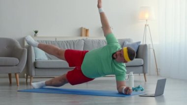 Dayanıklılık eğitimi. Parlak spor elbiseli şişman adam dizüstü bilgisayarda yoga dersi izliyor, yan tahtada duruyor.