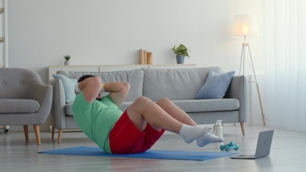 Problem med idrettstrening. Overvektig mann i lyse sportsklær som trener hjemme, som prøver å ta situps på gulvet – stockvideo