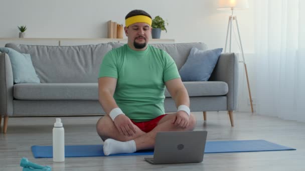 Pratique du yoga en ligne. Homme en surpoids paisible méditant sur le sol à la maison, allumant la leçon de yoga sur ordinateur portable — Video