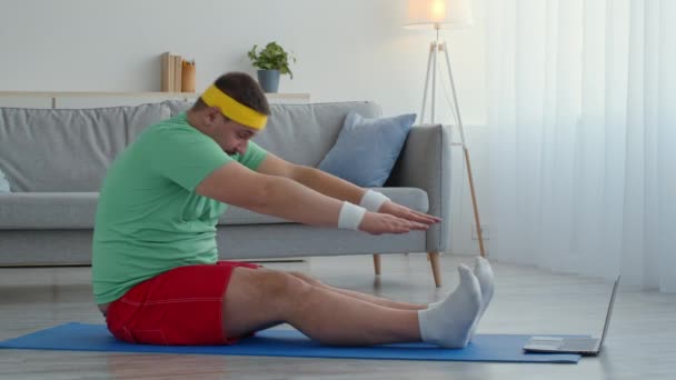 Problemen met lichaamsflexibiliteit. Overgewicht man doet stretching praktijk thuis, kijken naar online pilates les — Stockvideo