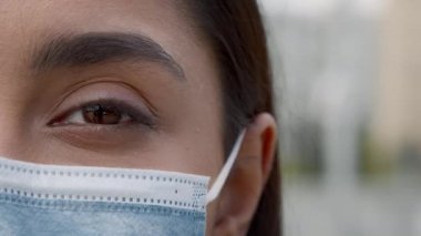 Yüzü maskeli kadın, dışarıda duran kameraya bakıyor, kırpılmış.