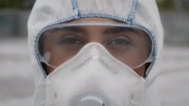 Tehlikeli madde giysisi giyen, koruyucu gözlük takan ve açık havada solunum cihazı takan bir tıp işçisi.