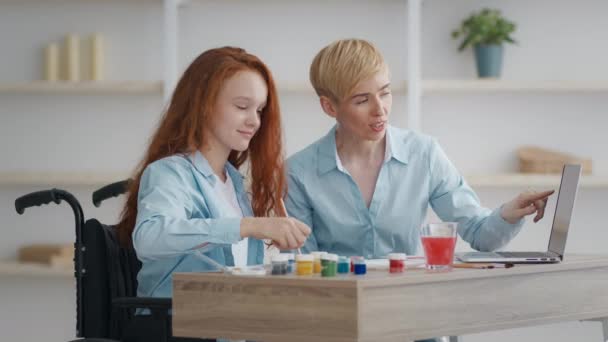 Pequena ruiva deficiente menina exercitando com a mãe em casa, assistindo vídeo tutorial no laptop e desenho em casa — Vídeo de Stock