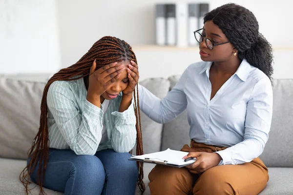 Upset black lady with nervous breakdown consulting psychologist, having session with counselor at clinic