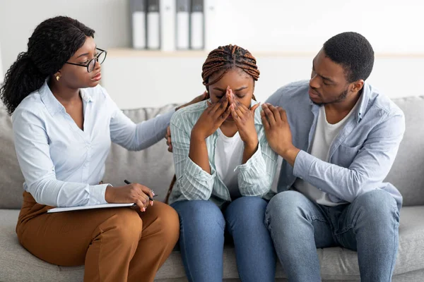 Jovem negra chorando no consultório de terapeutas, marido afetuoso apoiando-a com psicólogo profissional — Fotografia de Stock