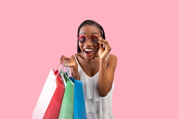 Gran venta estacional. Retrato de la joven mujer negra feliz posando con coloridas bolsas de compras sobre fondo de estudio rosa —  Fotos de Stock