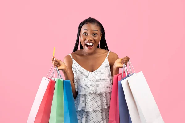 Mujer negra emocionada posando con tarjeta de crédito y bolsas de compras de colores, la compra de bienes sin contacto, la compra a la venta —  Fotos de Stock