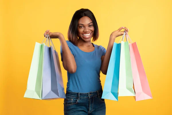 Mujer afroamericana alegre sosteniendo coloridas bolsas de compras, fondo amarillo —  Fotos de Stock