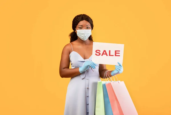 마스크와 장갑을 낀 흑인 여성 , SALE 사인을 보이고, 가판대를 들고, 코로나 바이러스를 사용하는 동안 할인 상품을 구매하는 모습 — 스톡 사진