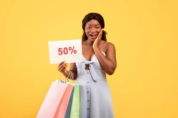 夏の大売り上げだ。興奮した若いアフリカ系アメリカ人女性がショッピングバッグとFIFTYパーセントオフサイン — ストック写真