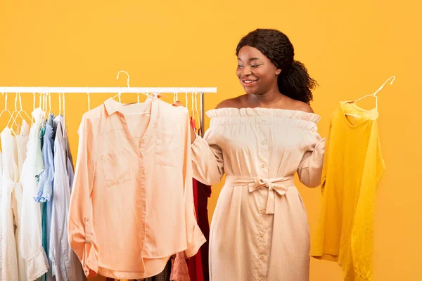 Yaz alışverişi. Mutlu siyahi kadın yeni kıyafetler arasında seçim yapıyor, elbise korkuluklarının yanında dikiliyor, gardırop seçiyor. — Stok fotoğraf