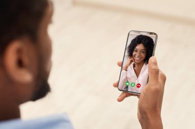Afrikalı Amerikalı bir adam kız arkadaşıyla görüntülü konuşma yapıyor. Uzaktan konuşma için akıllı telefonu kullanıyor.