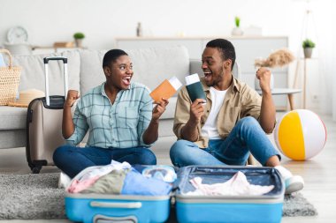 Siyah çift biletlerini tutuyor. Yumruklarını sallıyor. Tatilini Evde Kutluyor.