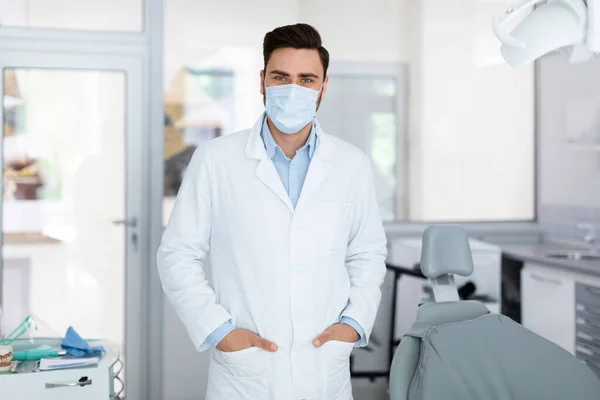 Jovem médico em máscara facial em pé na clínica odontológica — Fotografia de Stock
