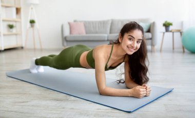 Evde fitness 'te kal. Güçlü Hintli kadın tüm vücut çalışmasını yapıyor, dirsek kalası pozisyonunda duruyor, içeride, panoramada.