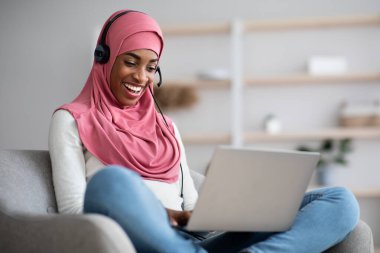 Keyifli siyahi kadın tesettürlü ve kulaklıklı Laptop 'ta giyinen
