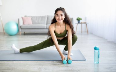 Genç Hintli kadın oturma odasında halterli germe egzersizleri yapıyor, panorama.