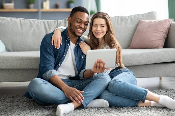 Jeunes conjoints interraciaux utilisant la tablette numérique ensemble tout en se reposant à la maison — Photo