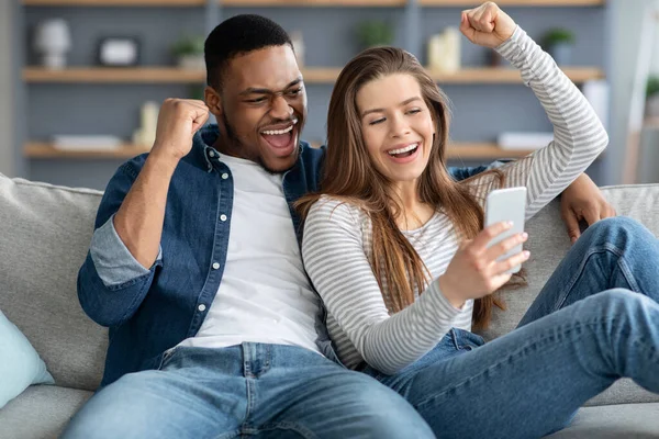 Ενθουσιασμένο διαφυλετικό ζευγάρι κοιτάζοντας οθόνη Smartphone και δικαιολογώντας με χαρά — Φωτογραφία Αρχείου