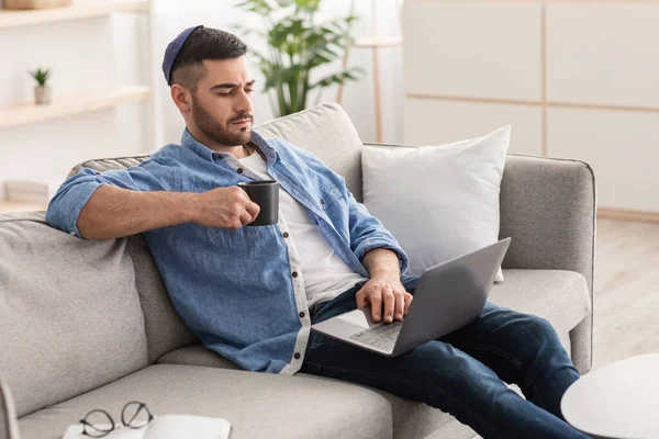 Jeune homme juif regarder la vidéo sur ordinateur, boire du café chaud — Photo