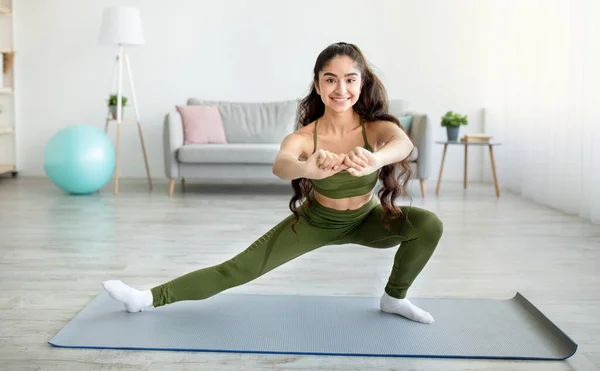 Inlåsning hemma träning. Sportig ung indisk dam sträcker benen på yogamattan i vardagsrummet, fritt utrymme — Stockfoto