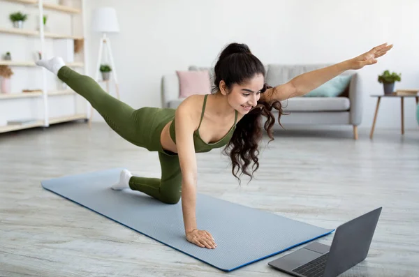 Online sports during covid lockdown. Millennial Indian woman exercising on mat, watching sports video on laptop at home — Stockfoto