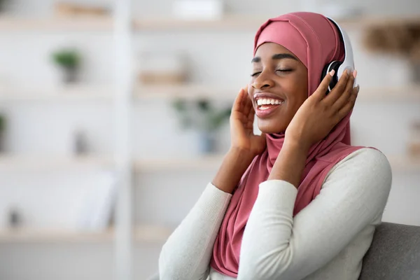 Tempo libero domestico. rilassato nero musulmano signora in hijab ascolto musica in cuffie — Foto Stock