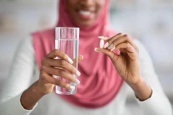 Black Woman In Hijab Taking Supplement Pill And Holding Glass Of Water