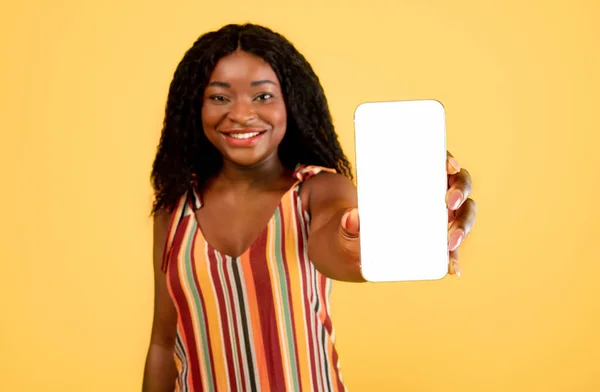Mujer negra mostrando teléfono celular con pantalla en blanco a la cámara sobre fondo naranja, maqueta para aplicación móvil o sitio web — Foto de Stock