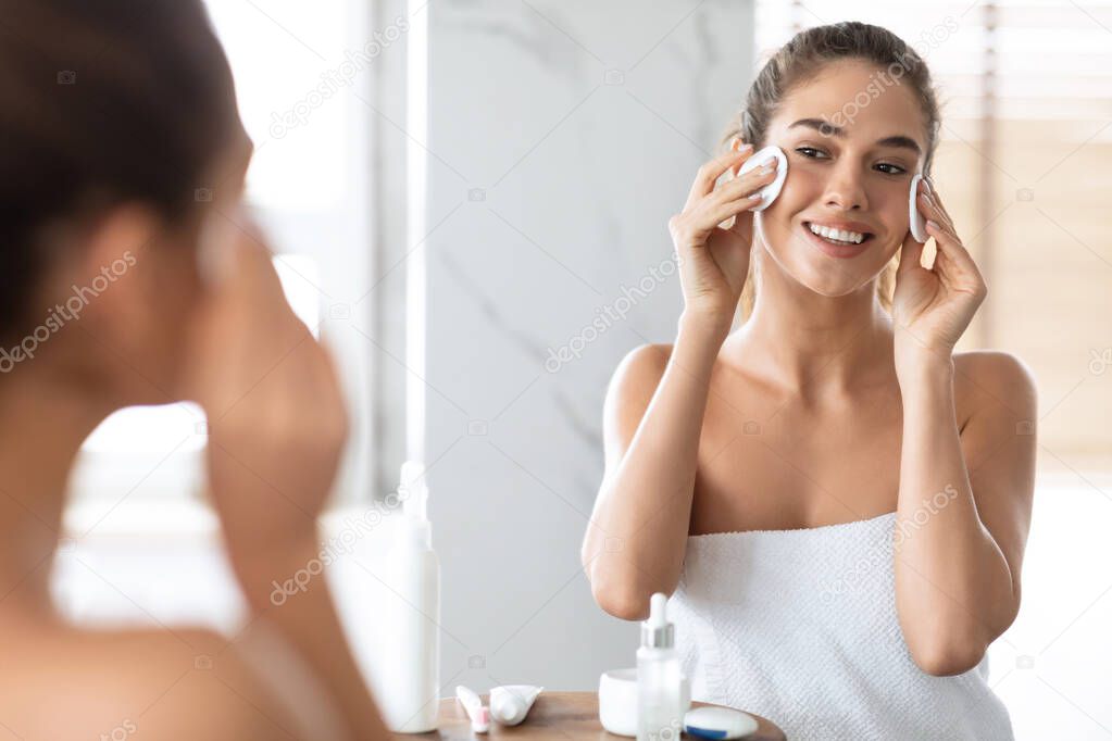 Happy Lady Cleansing Face With Cotton Pads Standing In Bathroom