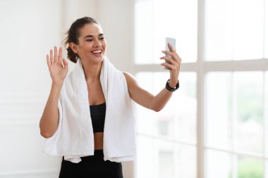 Genç kadın spor yapıyor ve akıllı telefon ekranına el sallıyor.