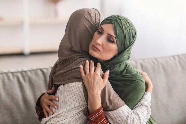 Senior Muslim Mother Hugging Unhappy Adult Daughter Wearing Hijab Indoor