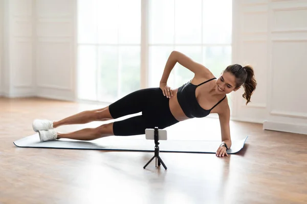 Jeune femme faisant planche latérale sur tapis avec téléphone — Photo