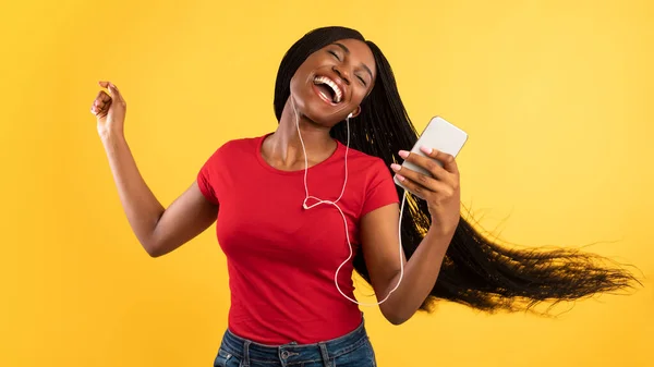 Dame noire écoutant de la musique sur Smartphone portant des écouteurs, fond jaune — Photo