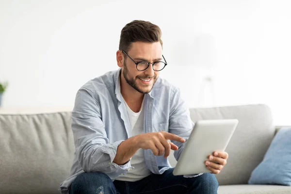 Freizeitkonzept. Glücklicher Mann mit digitalem Tablet, auf Couch im Wohnzimmer sitzen, Raum kopieren — Stockfoto
