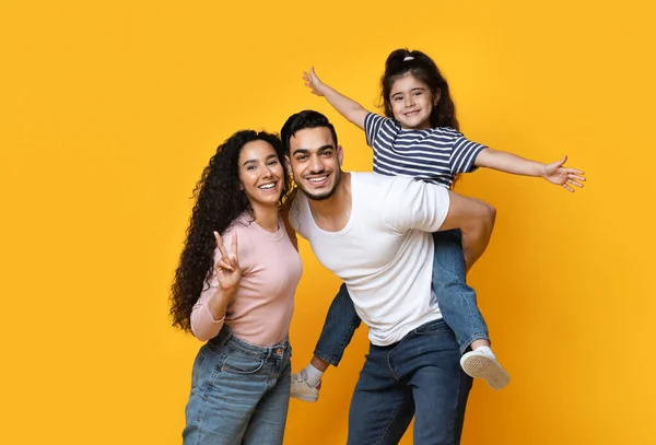 Retrato de alegre família árabe com pequena filha posando sobre fundo amarelo — Fotografia de Stock