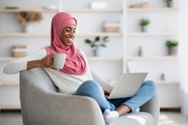 Siyah kadın evde dizüstü bilgisayar ve kahveyle dinleniyor.