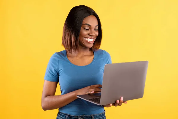 Happy black woman using laptop browsing internet over yellow background — Stock Photo, Image
