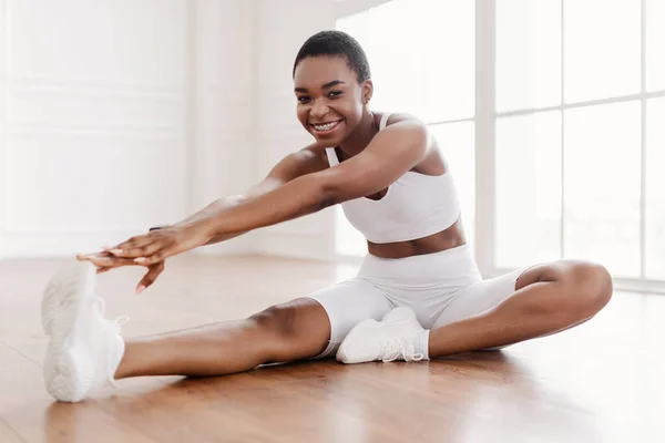 Fröhliche schwarze Frau in Sportbekleidung, die das Bein auf dem Boden ausstreckt — Stockfoto