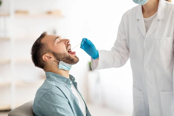 Médico fazendo teste de coronavírus oral PCR para homem jovem na clínica. Millennial cara submetido a procedimento de diagnóstico vívido — Fotografia de Stock