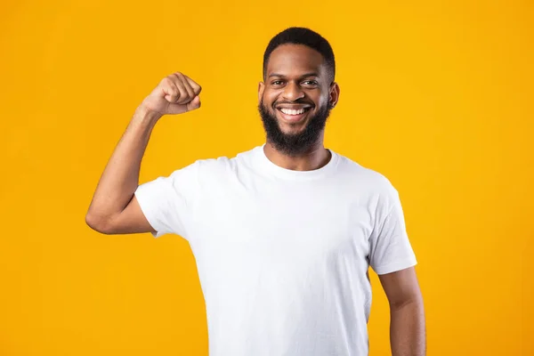 Alegre negro chico mostrando bíceps músculos posando en amarillo fondo —  Fotos de Stock