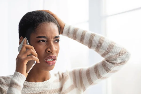 Vem som ringer. Förvirrad afrikansk dam talar på mobiltelefon och berörande huvud — Stockfoto